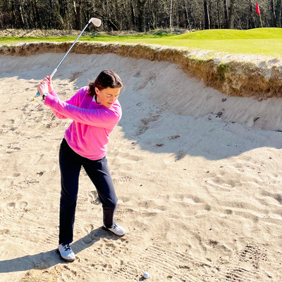 Golferin im Bunker, gekleidet im pinken Kaschmir Pullover